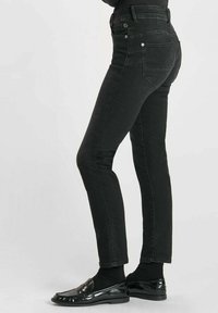 Jean en denim noir avec une coupe slim, présentant des poches arrière, une taille mi-haute et un léger délavage. Associés à des mocassins noirs brillants.