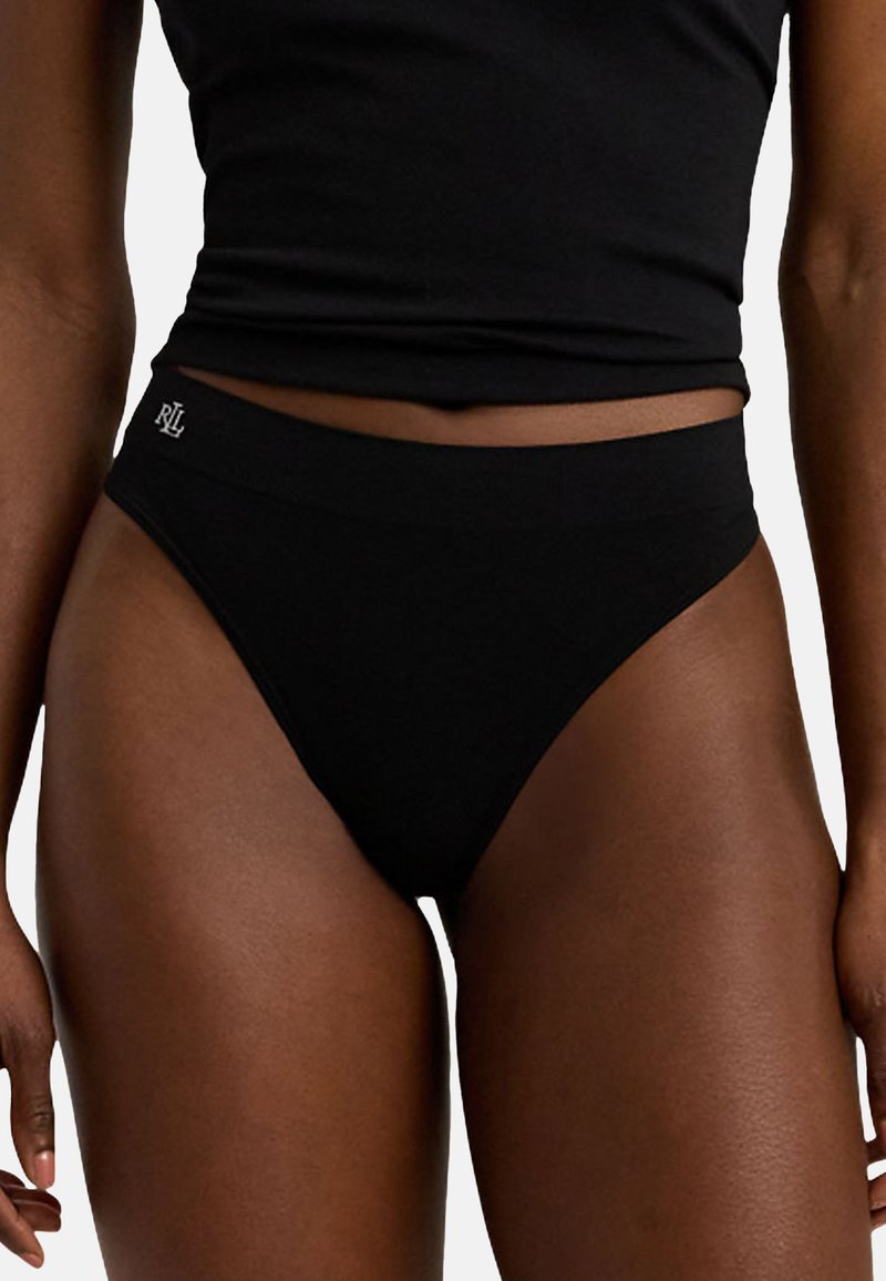 Zwarte high-waisted thong van zacht materiaal, met een elastische tailleband en een subtiele logodetail aan de voorkant. Gladde textuur en naadloos ontwerp.