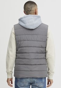 Grå puffy vest med horisontal quilting, med en grå hettegenser under, kombinert med lyseblå jeans.