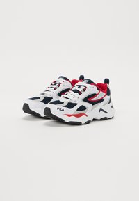 Białe i granatowe sneakersy sportowe z czerwonymi akcentami, siatkowy wierzch, zaokrąglony czubek, gruba podeszwa i wyraźne detale logo po bokach i na języku.