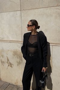 Svart skräddarsydd kavaj över en genomskinlig svart topp med spetsdetaljer, i kombination med högmidjade svarta byxor och en strukturerad svart handväska.