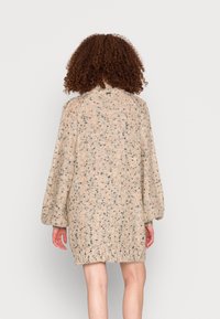 Großer Strickpullover in Beige mit schwarzen und pfirsichfarbenen Sprenkeln, ausgestattet mit einem hohen Kragen und Ballonärmel, abgeschlossen mit einem gerippten Saum.