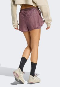 Ljubičaste, lagane hlačice s elastičnim pojasom i stražnjim džepom. Nošene s crnim čarapama i bež sportskim cipelama.