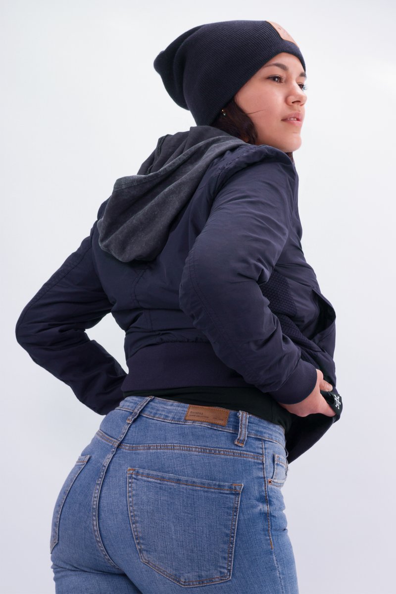 Marinebombenjacke mit grauem Kapuzenfelt, kombiniert mit einer blauen Jeans. Die Jacke hat elastische Bündchen und einen elastischen Saum. Das Model posiert mit den Händen auf den Hüften.