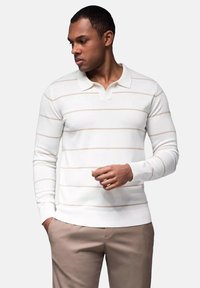 Witte polo met lange mouwen en subtiele horizontale roze strepen, voorzien van een kraag en ribgebreide manchetten, gecombineerd met lichtbeige broeken.