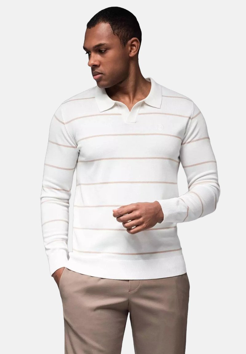 Witte polo met lange mouwen en subtiele horizontale roze strepen, voorzien van een kraag en ribgebreide manchetten, gecombineerd met lichtbeige broeken.