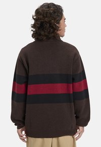 Brauner Pullover mit kräftigen horizontalen Streifen in Rot und Schwarz. Weicher Stoff mit lässigem Schnitt und gerippten Bündchen und Saum.