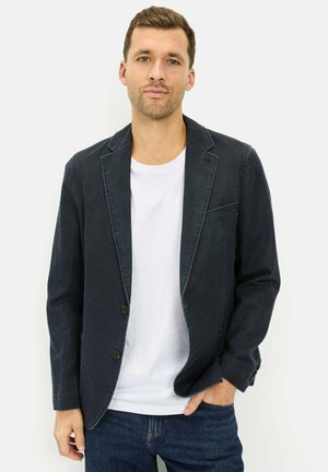 Marineblaues Blazer mit strukturierter Oberfläche, zwei Knöpfen, Reverskragen und einer Brusttasche, getragen über einem weißen T-Shirt.