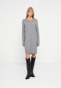 Robe en tricot gris à manches longues et ourlet côtelé, associée à des bottes noires jusqu'aux genoux. Sa texture douce et sa coupe décontractée augmentent le confort.