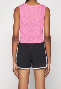 Top sin mangas de color rosa con un diseño texturizado, combinado con pantalones cortos negros que tienen rayas blancas en los laterales. Enfocado en la comodidad y la movilidad.