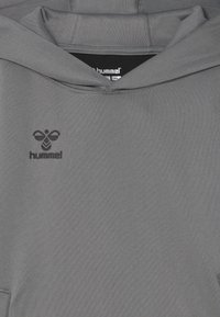 Grå hoodie med texturerad tyg, med huva och en svart broderad logotyp på bröstområdet. Enkel och funktionell design.