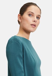 Turkusowa sukienka z tkaniny o dopasowanej górze, okrągłym dekolcie i bezszwowych rękawach. Gładka tekstura z delikatnymi detalami krawieckimi.