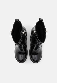 Bottines en cuir verni noir avec un bout arrondi, des fermetures éclair latérales et des coutures blanches contrastées le long de la semelle. Texture lisse partout.