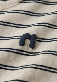 Stribet beige stof med mørkeblå vandrette striber, der har et mørkeblåt blødt gummilogo formet som et "n" på forsiden.