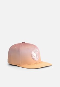 Snapback cap in gradient peach and blush, featuring a raised white logo on the front, flat brim, and textured fabric.