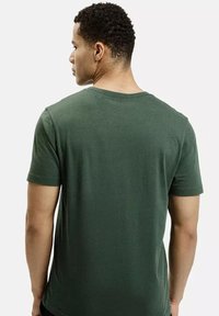 Ciemnozielona koszulka z krótkim rękawem o klasycznym okrągłym dekolcie, wykonana z miękkiej bawełny, o gładkiej i równej fakturze.