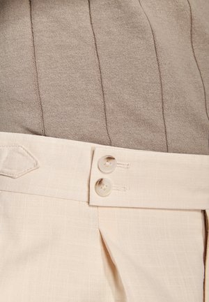 Pantalones beige de talle alto con dos botones color crema en la cintura, combinados con un top de punto acanalado color topo.