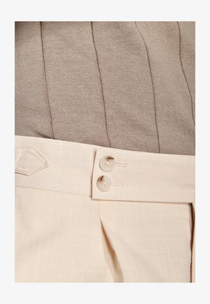 Pantalones beige de talle alto con dos botones color crema en la cintura, combinados con un top de punto acanalado color topo.