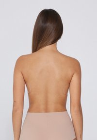 Zadní pohled na ženu v tělovém hladkém body. Doplněk zahrnuje kulaté silikonové podložky na ramenech a hladký textilní materiál.