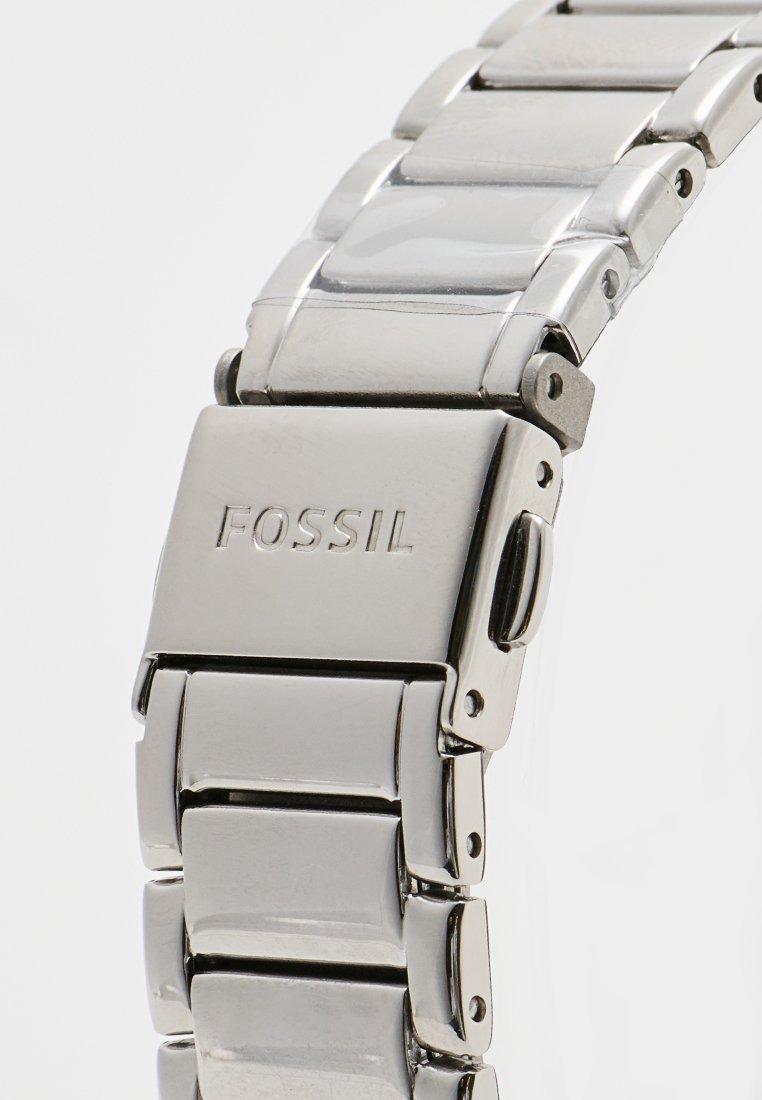 Bracelet de montre en acier inoxydable argenté avec finition polie, comportant des maillons rectangulaires et un fermoir marqué "FOSSIL". Texture lisse et conception durable.