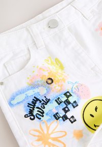 Pantaloncini bianchi di cotone con schizzi di vernice di vari colori, tra cui giallo, rosa e blu, con una faccina sorridente e motivi floreali.