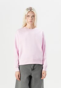 Felpa di cotone rosa con colletto rotondo, spalle cadenti e polsini a costine, abbinata a pantaloni grigi scuri morbidi.