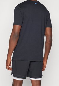 Czarna koszulka krótki rękaw, z mieszanki bawełny, z niebieskim logo z tyłu. Połączona z czarnymi szortami sportowymi, z białym wykończeniem i akcentami po bokach.