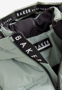 Jachetă puffer verde deschis, cu căptușeală interioară neagră, având fermoar frontal și o etichetă din material cu brandul "BAKER by Ted Baker."