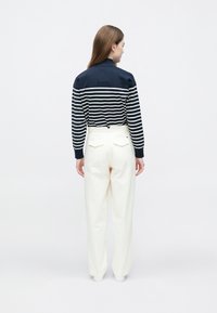 Marineblå og hvitstripet langtermet topp kombinert med høytlivede kremfargede bukser. Har en avslappet passform og baklommer på buksene.