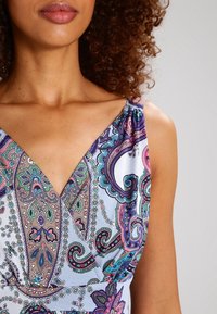 Mekko, jossa on kuviollinen V-pääntie, värikäs paisley-kuviointi purppuran, vihreän ja sinisen sävyissä vaalealla taustalla, valmistettu sileästä kankaasta.