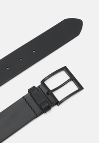 Cintura in pelle nera con una texture liscia, fibbia metallica rettangolare e cinque fori di regolazione. Presenta dettagli firmati vicino alla fibbia.