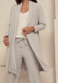 Lichtgrijze geribbelde gebreide cardigan met een open voorkant, gecombineerd met bijpassende jogpants met koord, en een crèmekleurige getailleerde top. Soepele textuur.