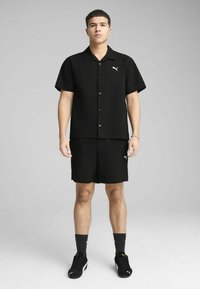 Czarny dwuczęściowy zestaw składający się z koszuli z krótkim rękawem i szortów, oba wykonane z teksturowanej tkaniny. Logo na koszulce i szortach.