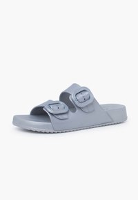 Light grey slide sandals featuring dual adjustable straps with large buckles, a smooth material, and a textured, ridged sole for grip.