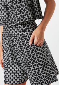 Shorts noirs avec un motif géométrique blanc, fabriqués en tissu léger, comprenant une poche latérale et un design de ceinture ajustée.