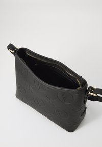 Sac à épaule en cuir noir avec un motif en logo embossé, fermeture zippée et quincaillerie dorée. Intérieur doublé de tissu noir.