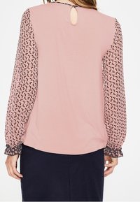 Blusa a maniche corte in morbido tessuto rosa, con maniche lunghe trasparenti e decorate, dettaglio a forma di chiave sul retro e polsini elasticizzati.