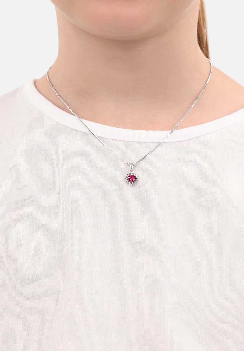 Collana in argento con pendente a forma di cuore in pietra rosa, circondato da piccole pietre trasparenti, indossata sopra una maglietta bianca.