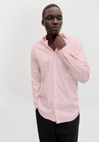 Ροζ ανοιχτόχρωμο πουκάμισο με μακριά μανίκια, κλασικό γιακά και κουμπωτά μανσέτα, συνδυασμένο με σκούρο παντελόνι. Λείο ύφασμα, εφαρμοστή γραμμή.