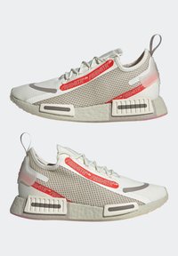 Ljusgrå sneakers med en texturerad mesh-överdel, röda och silverdetaljer, unik sula-design och präglade detaljer på hälen och sidorna.