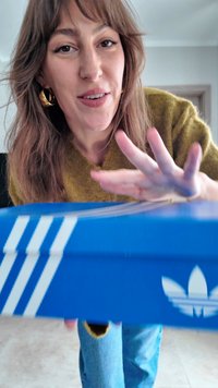 Niebieskie kartonowe pudełko z białymi trzema paskami i logo Adidas. Pudełko jest częściowo otwarte, ukazując teksturowane wnętrze.