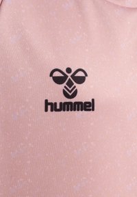 Ljust rosa tyg med en subtil textur, med en svart Hummel-logotyp och en design av en stiliserad bi ovanför varumärket.