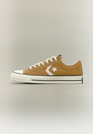 Lage bruine canvas sneaker met witte veters, sterrenlogo aan de zijkant, witte rubberen neuskap en witte zool met zwarte strepen.