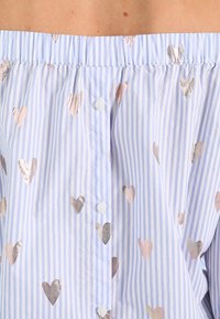 Ljusblå off-shoulder topp med vita vertikala ränder, dekorerad med metalliska hjärtan i roséguld och silver. Har knappstängning.