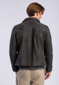 Chaqueta de cuero gris oscuro con un cuello estructurado, detalle de costura en la parte posterior y un parche de logo en el cuello. Acabado texturizado con un aspecto suave.
