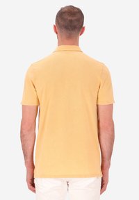 Polo shirt giallo con maniche corte, colletto e tessuto di cotone morbido. Presenta un orlo dritto e spacco laterale per il comfort.