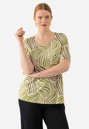 Camiseta de manga corta y cuello en V en tela beige con patrones de hojas verdes en forma de olas. Textura suave, corte relajado. Combínala con pantalones oscuros.