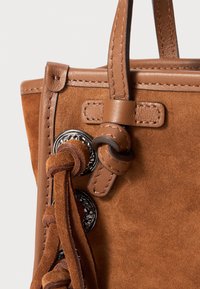 Sac à main en suede marron avec des accents en cuir, présentant des détails en franges et une quincaillerie métallique. Texture lisse et forme structurée.