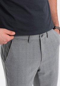 Pantaloni grigi a motivo houndstooth con vestibilità su misura, tasche laterali e chiusura con bottone. Il tessuto ha una consistenza liscia.