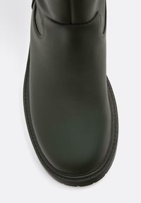 Černá gumová bota s kulatou špičkou, hladkým povrchem a prošitými detaily podél okraje. Klasický design se bočními otvory.